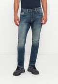 Mann trägt verwaschene blaue Jeans, schwarze Sportschuhe mit grauen Akzenten und ein dunkles Shirt vor einem weißen Hintergrund.