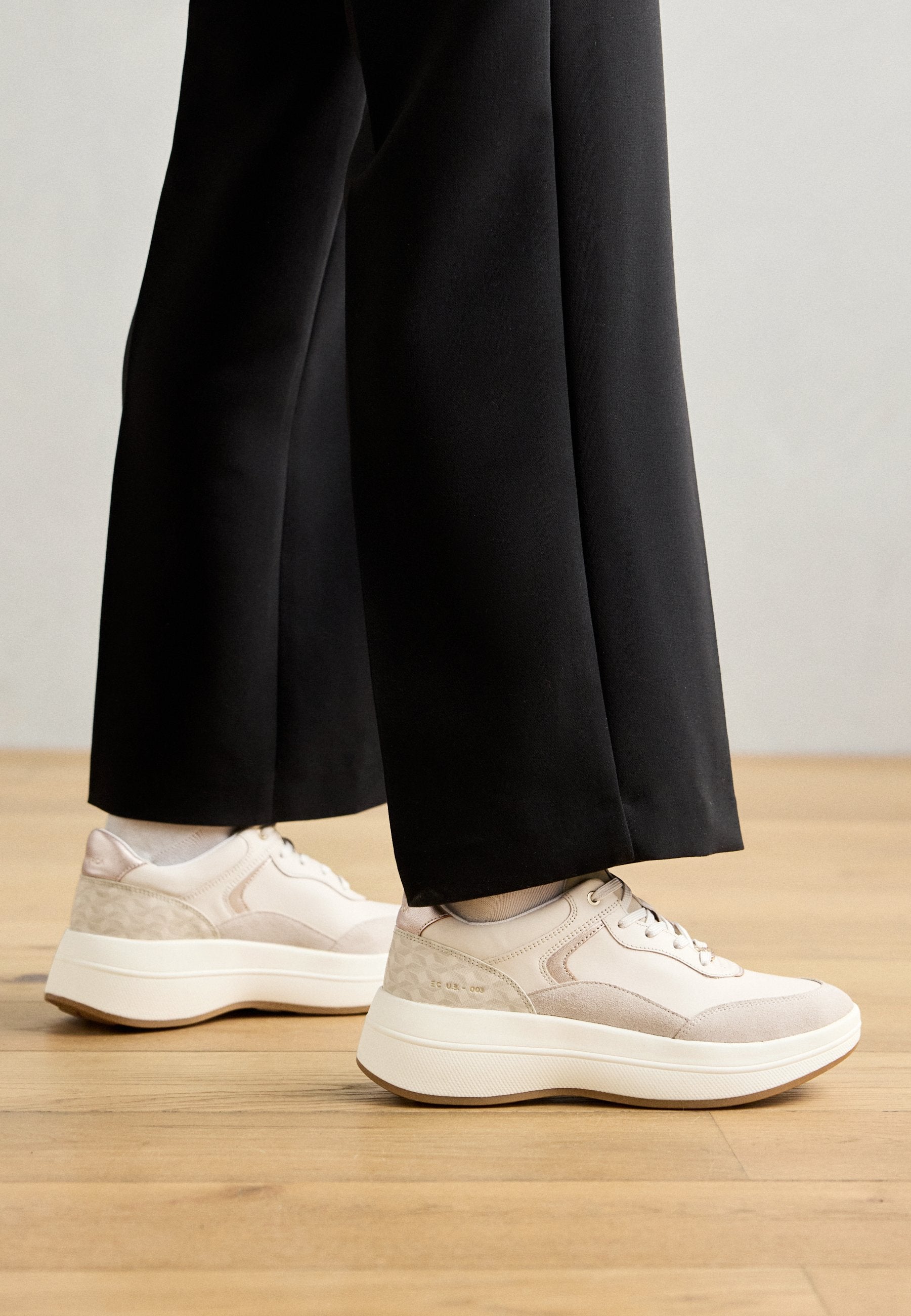 Sneaker aus einer Kombination von hellrosa und beige Materialien, mit einem strukturierten Fersenbereich, runder Zehenpartie und dicker weißer Sohle.