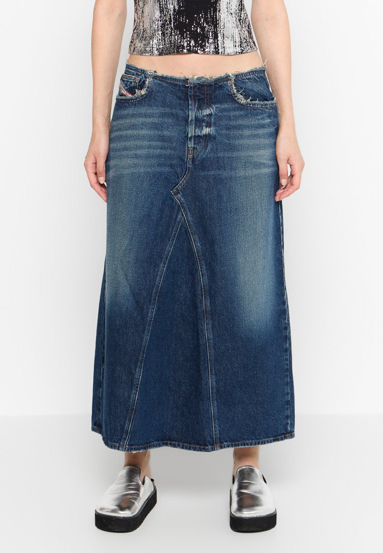 Eine Frau trägt einen langen, dunkelblauen Jeansrock mit ausgefranstem Bund, kombiniert mit silbernen, metallic-farbenen Slip-On-Schuhen und einem cropped Top.