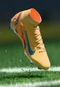 Helles gelbes Fußballschuh mit blauen Akzenten, strukturierter Oberseite und sichtbaren Schnürsenkeln. Über dem Gras positioniert, um eine dynamische Hebung zu zeigen.