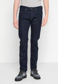 Dunkelblaue Denim-Jeans mit Slim-Fit, Fünf-Taschen-Design und einem dezenten Logo auf der vorderen Tasche. Kombiniert mit grauen Sneakers.