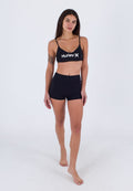 Schwarzes Sport-Bralette mit verstellbaren Trägern und weißem "Hurley"-Logo, kombiniert mit hochgeschnittenen schwarzen Shorts. Glatte Textur, figurbetontes Design.