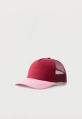 Bordeauxrote und rosa Trucker-Cap mit Netzrücken und dezentem Text auf dem Frontpanel, vor einem einfarbigen hellen Hintergrund.