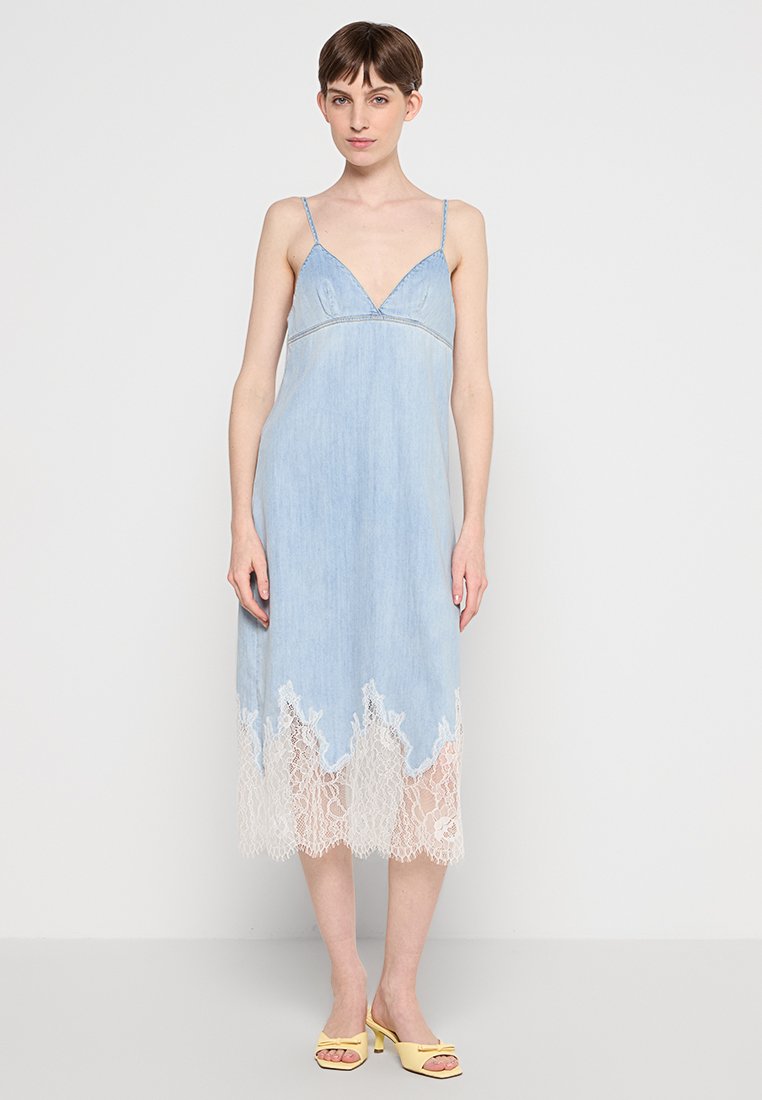 Hellblaues Denimkleid mit Spitzenbesatz am Saum, ausgestattet mit einem V-Ausschnitt und dünnen Trägern. Glatte Textur, mittellanges Design.