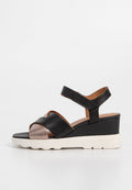 Schwarze und metallische Wedge-Sandalen mit offenen Zehen, gekreuzten Riemen, strukturiertem Leder und einer weißen Gummisohle mit gewelltem Design.