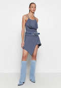Graues ärmelloses Kleid mit drapiertem Ausschnitt, asymmetrischem Saum und Denim-Gürtel. Kombiniert mit hohen, hellblauen, von Vintage inspirierte Stiefeln.