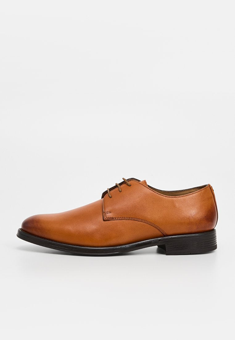Brauner Lederschuh mit glatter Oberfläche, rundem Zehenbereich und dreifacher Ösen-Schnürung. Verfügt über eine flache, schwarze Gummisohle und kontrastierende Nähte.