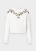 Weißes, kurzes Sweatshirt mit langen Ärmeln, das ein Ketten- und Herzmuster aus metallischem Faden entlang des Halsausschnitts und der Schultern aufweist.