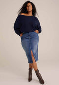 Marineblaues Oversized-Sweatshirt mit schulterfreiem Design, kombiniert mit einem denimbasierten Bleistiftrock mit Schlitz vorne. Braune Stiefeletten.