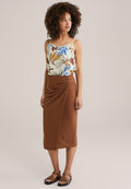 Leichtes Tanktop mit floralen Mustern in Creme, kombiniert mit einem braunen, knielangen, drapierten Rock mit Knopfdetails. Schwarze Sandalen mit Riemchen.