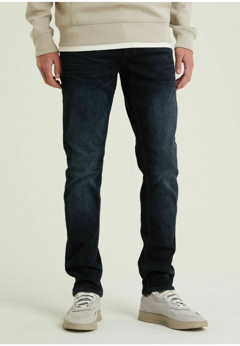 Dunkelblaue Jeans im Slim Fit mit klassischem Fünf-Taschen-Design und subtilen Ausbleichungen, kombiniert mit hellen Sneakers.