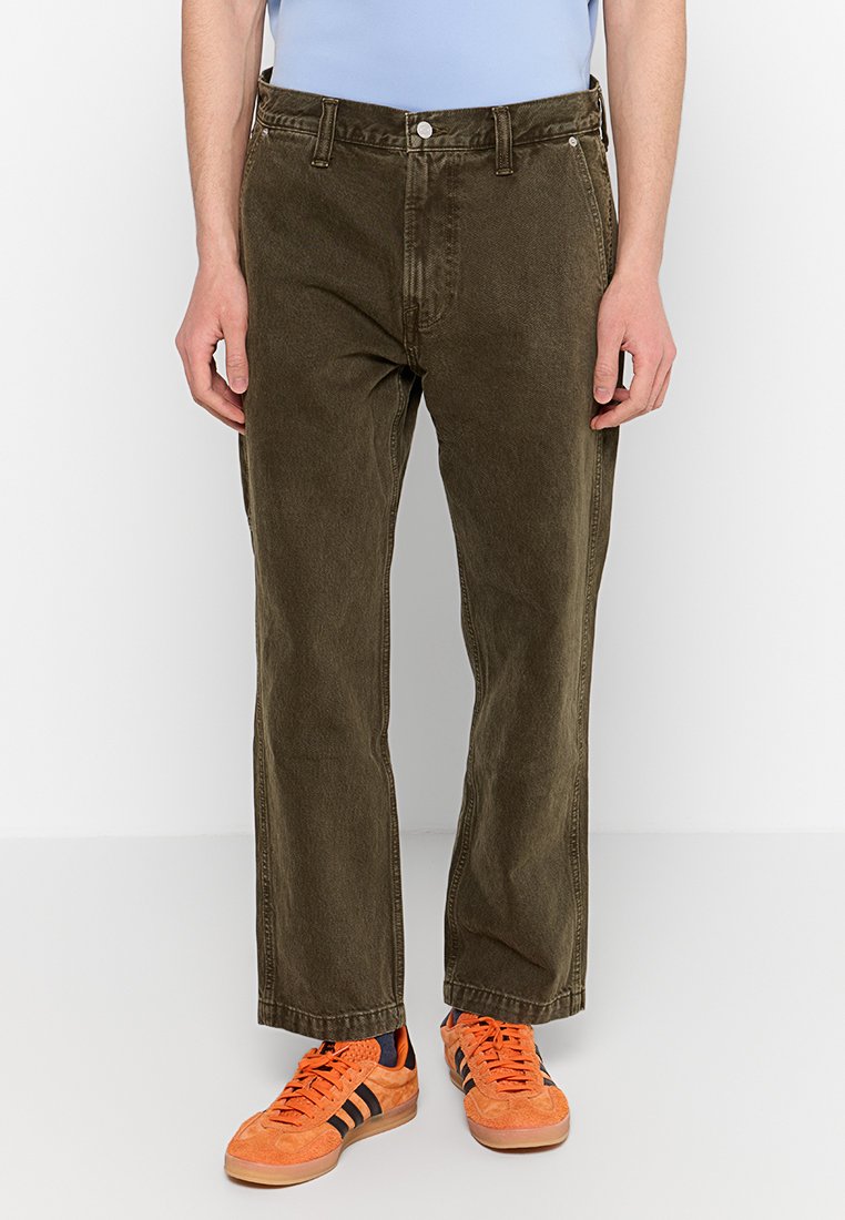 Olivgrüne Cordhosen mit geradem Bein-Design, ausgestattet mit einem Knopfverschluss und Gürtelschlaufen. Getragen mit orangen Sneakers.