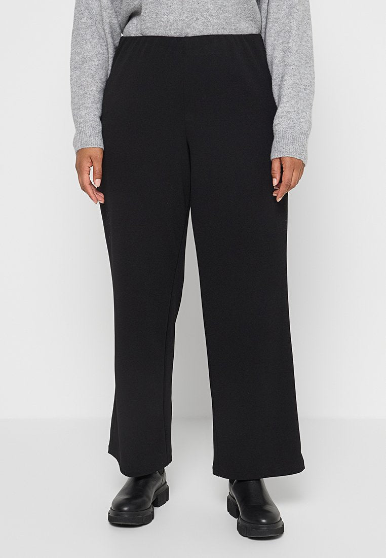 Schwarze, weite Hosen aus weichem Stoff mit einem elastischen Bund. Kombiniert mit einem hellgrauen Pullover und schwarzen Stiefeln bis zum Knöchel.