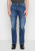 Mann trägt blaue Jeans mit geradem Schnitt und schwarze Lederschuhe, steht vor einem schlichten weißen Hintergrund.