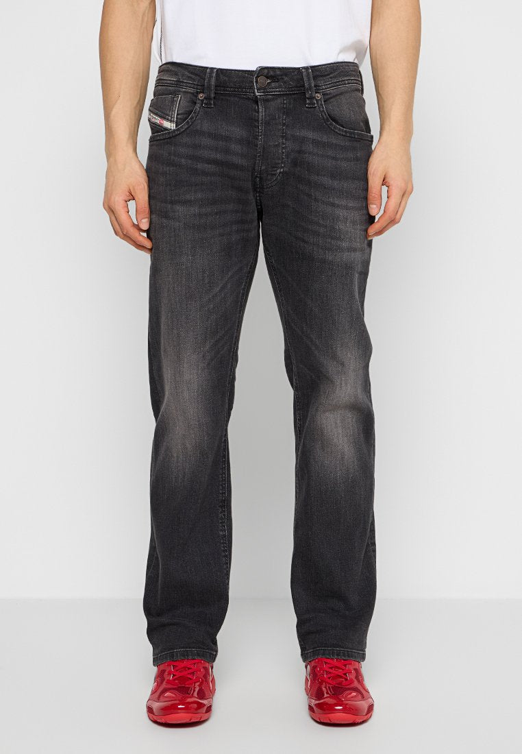 Dunkelgraue Jeans aus Denim mit leichtem Verblassen, mit fünf Taschen und einem Knopfverschluss. Kombiniert mit knallroten Schuhen.