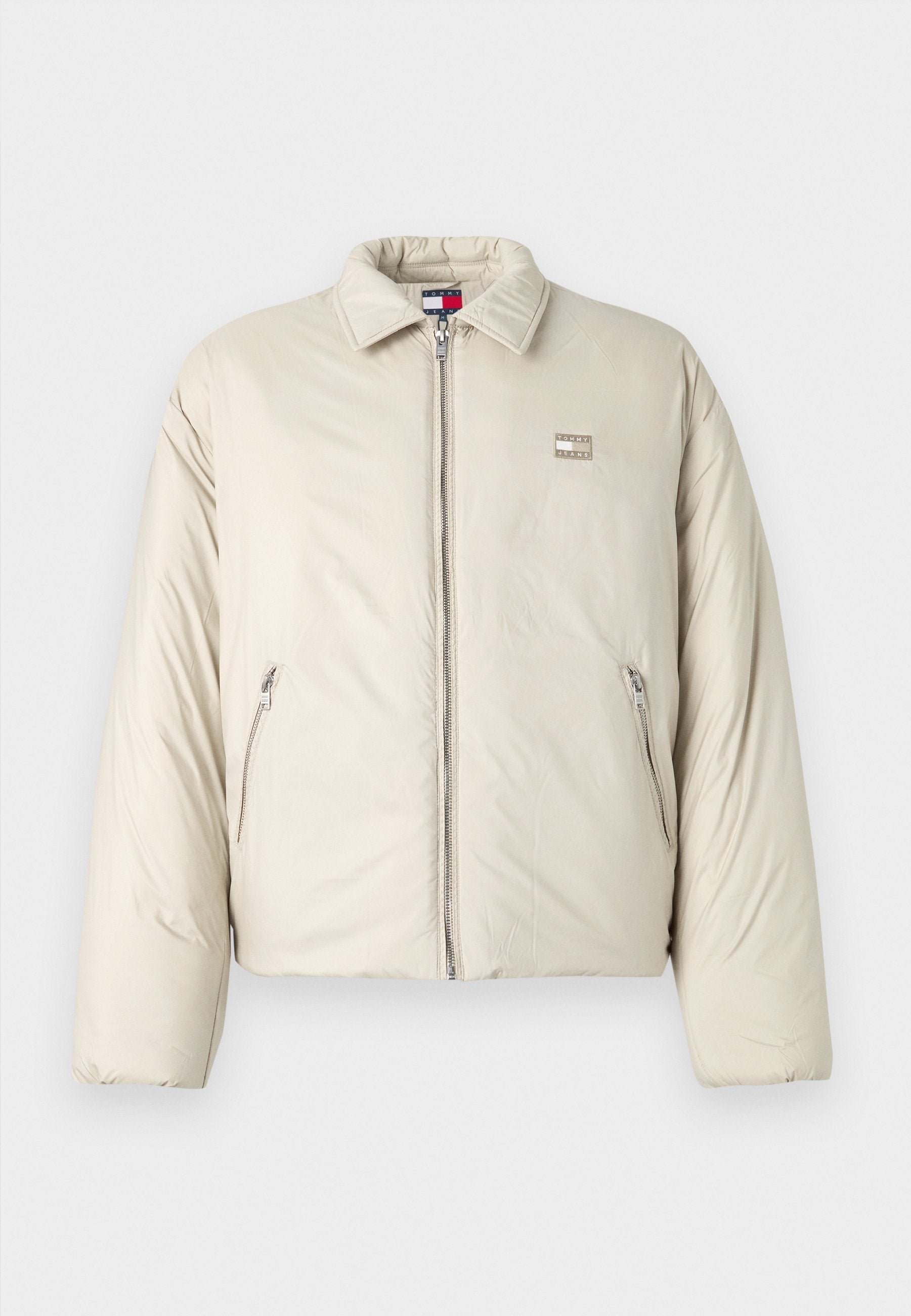 Beige Daunenjacke mit Stehkragen, Frontreißverschluss und zwei Seitentaschen. Mit einem Logopatch auf der linken Brust.