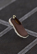 Brauner Slipper mit strukturiertem Obermaterial und kontrastierender hellerer Sohle, ausgestattet mit einer Zuglasche und dezentem Branding an der Seite.