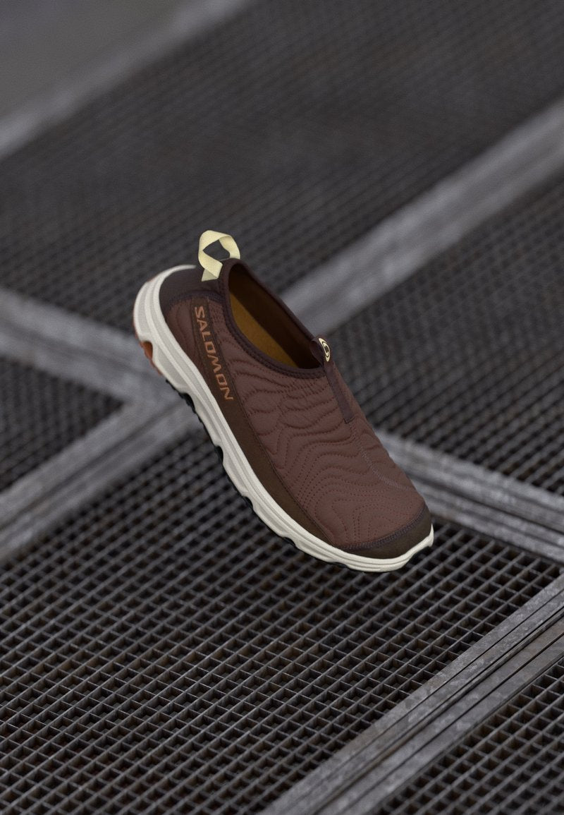 Brauner Slipper mit strukturiertem Obermaterial und kontrastierender hellerer Sohle, ausgestattet mit einer Zuglasche und dezentem Branding an der Seite.
