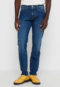 Dunkelblaue Denim-Jeans im geraden Schnitt mit Knopfverschluss, Gürtelschlaufen und gestickten Akzenten an den Taschen. Getragen mit gelben Schuhen.