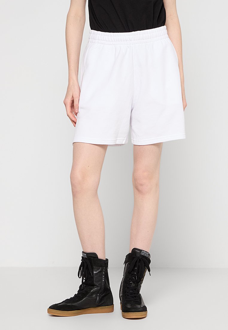Weiße Shorts mit elastischem Bund und entspannter Passform, die eine glatte Textur haben und keine sichtbaren Muster aufweisen, kombiniert mit schwarzen High-Top-Boots.