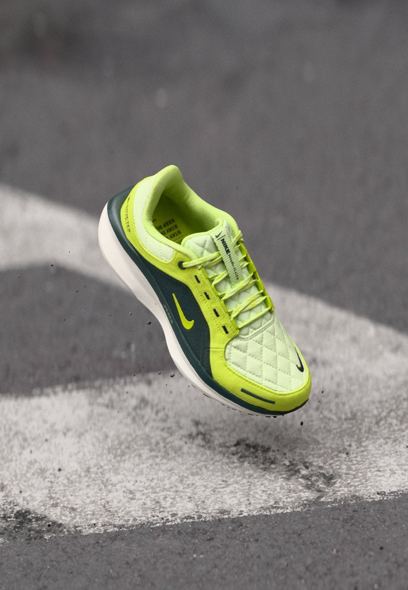 Limettengrüne Sneaker mit gestepptem Obermaterial, dunkelgrünen Akzenten, weißer Sohle und sichtbarem schwarzem Nike-Swoosh; verfügt über ein schnürbares Design und eine strukturierte Oberfläche.