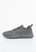 Grauer Sportschuh aus Synthetikmaterial, mit strukturiertem Obermaterial, gepolstertem Kragen und einer dicken, wellenmusterförmigen Sohle.