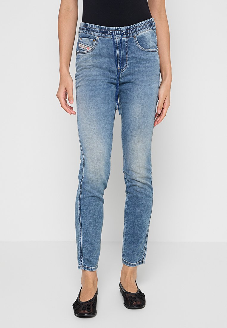 Schmal geschnittene blaue Jeans mit verwaschenem Frontteil, elastischem Bund, Kordelzug und getragen mit schwarzen Ballettschuhen auf einem hellen Hintergrund.