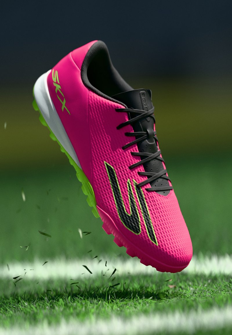Helle rosa Fußballschuhe mit schwarzen Schnürsenkeln und grüner Sohle, die Gras auf einem Kunstrasenplatz nahe einer weißen Feldlinie aufwirbeln.