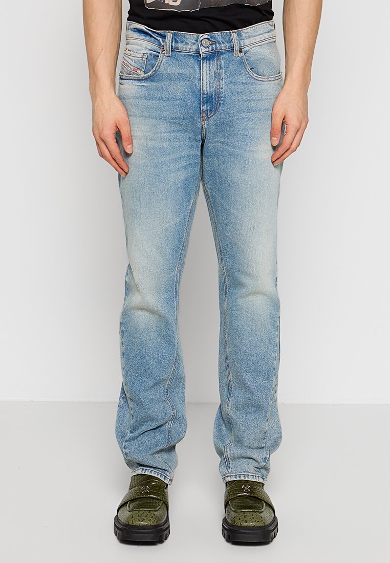 Helles blaues Denim-Jeans mit lockerer Passform, ausgewaschenem Finish, fünf Taschen und geradem Bein, gezeigt mit grünen Schuhen.