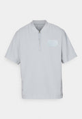 Hellgraues Poloshirt mit halbem Reißverschluss und kurzen Ärmeln, aus strukturiertem Stoff mit einem dezenten Logopatch auf der Brust.