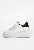Weiße Leder Sneaker mit schwarzer Fersenakzent, dicker Plateausohle, silbernen Ösen und goldenen Logo-Details an der Seite. Glatte Textur.