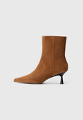 Braune Wildleder-Ankle-Boots mit spitz zulaufender Zehenpartie und konisch geformtem, schwarzem Absatz. Glatte Textur mit minimalen Details und einer klaren Silhouette.