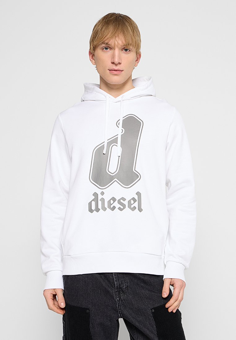 Junger Mann trägt einen weißen Diesel-Hoodie mit einem großen dunkelgrauen "d"-Logo und schwarze Jeans, steht vor einem schlichten weißen Hintergrund.