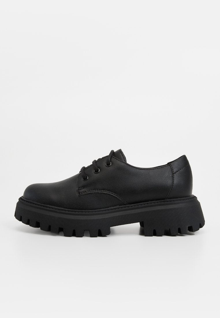 Schwarze Leder Schnürschuhe mit dickem, robustem Sohlenprofil, entworfen für Langlebigkeit und Stil auf einfarbigem Hintergrund.