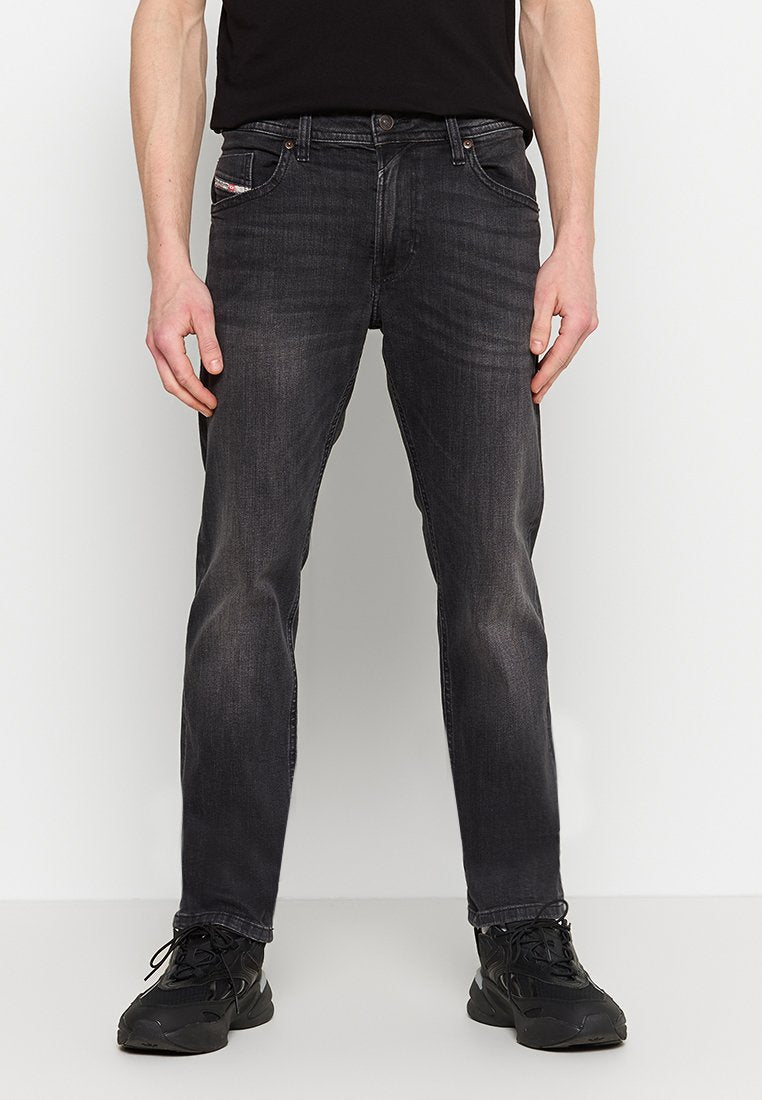 Schwarze Jeans aus Denim mit gerader Passform, Fünf-Taschen-Design und dezenten Used-Effekten. Getragen mit einem schwarzen T-Shirt und dunklen Sneakern.
