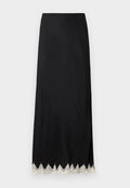 Schwarzer Maxi-Rock aus glattem Stoff mit hohem Schlitz und kunstvoller weißer Spitzenverzierung am Saum, mit geradem Schnitt und minimalistischem Design.