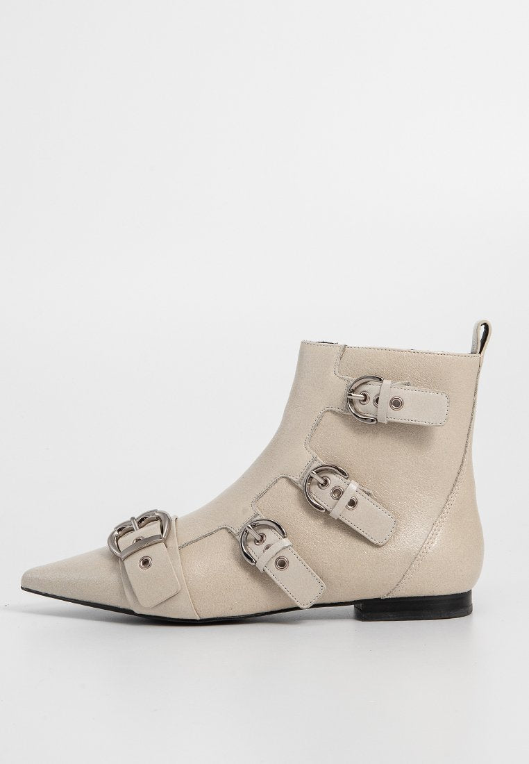 Beige Stiefelette mit spitzem Fuß, die mit vier Schnallenakzenten, einer strukturierten Oberfläche und einem niedrigen schwarzen Absatz versehen ist. Glattes Material überall.