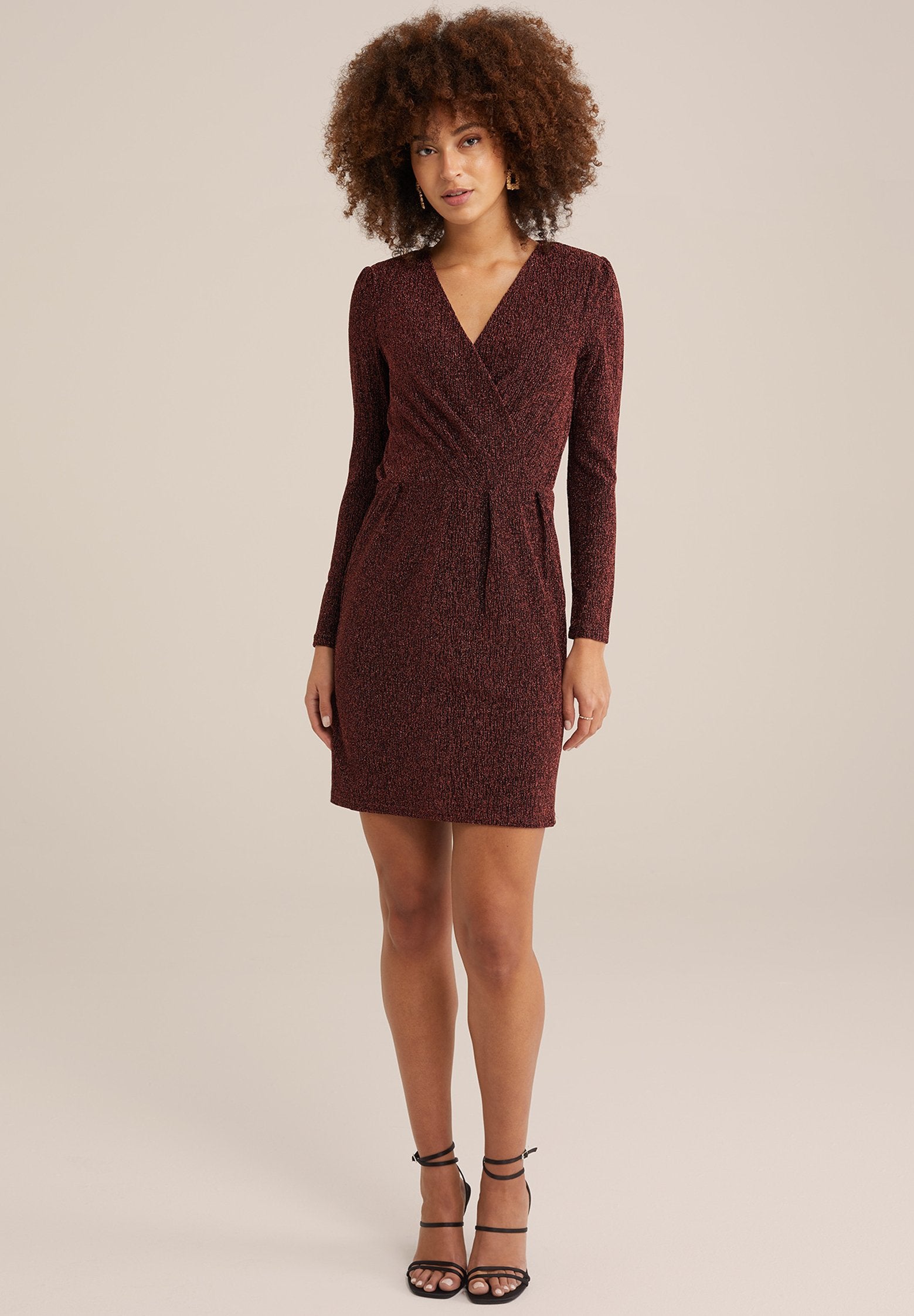 Bordeauxfarbene Wickelkleid mit langen Ärmeln, strukturiertem Stoff, taillierter Passform und einem kurzen Rock. Kombiniert mit schwarzen Riemchen-High Heels.