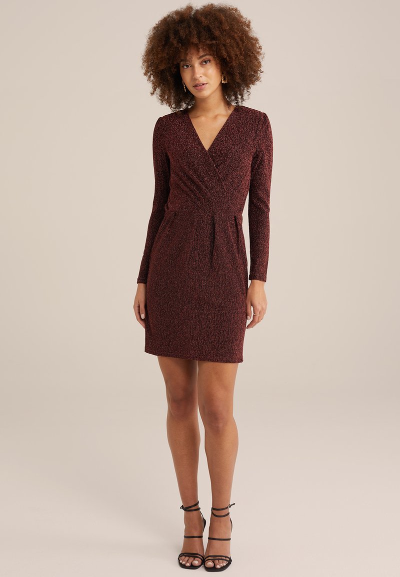 Bordeauxfarbene Wickelkleid mit langen Ärmeln, strukturiertem Stoff, taillierter Passform und einem kurzen Rock. Kombiniert mit schwarzen Riemchen-High Heels.