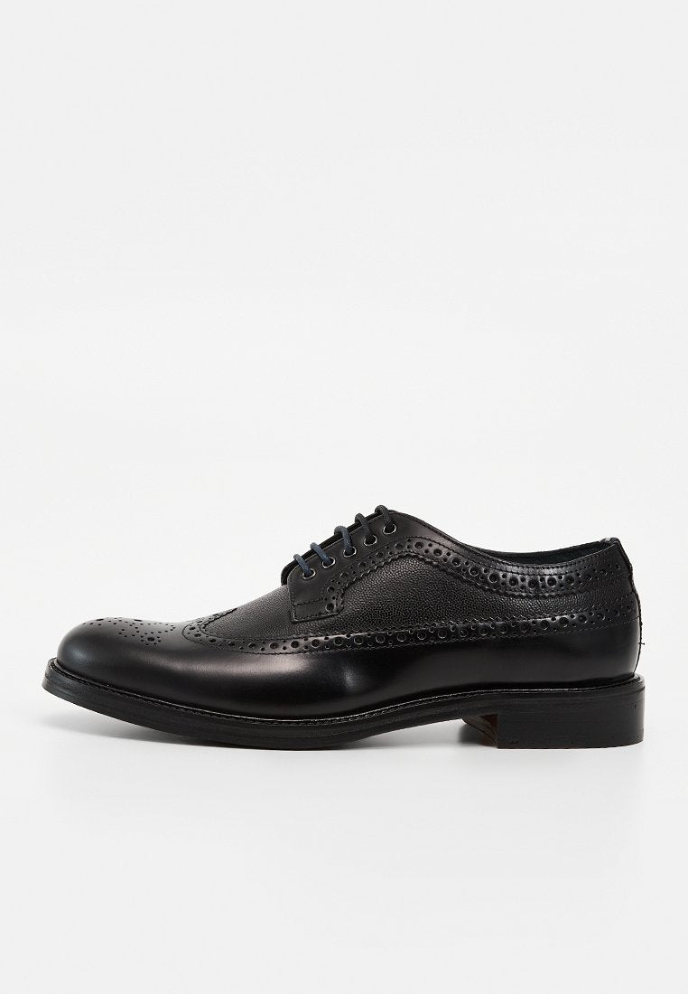 Schwarzer Lederschnürschuh mit Brogue-Design, perforierten Ziermustern und schwarzen Schnürsenkeln, von der Außenseite vor weißem Hintergrund gezeigt.