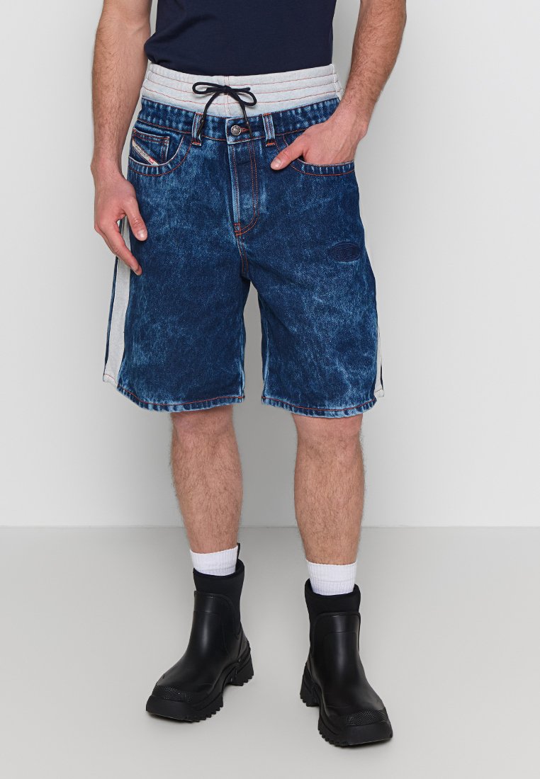 Denim-Shorts mit einem verblassten blauen Finish, ausgestattet mit einem Kordelzug-Bund, seitlichen Taschen und kontrastierenden seitlichen Akzenten. Getragen mit schwarzen Stiefeln.