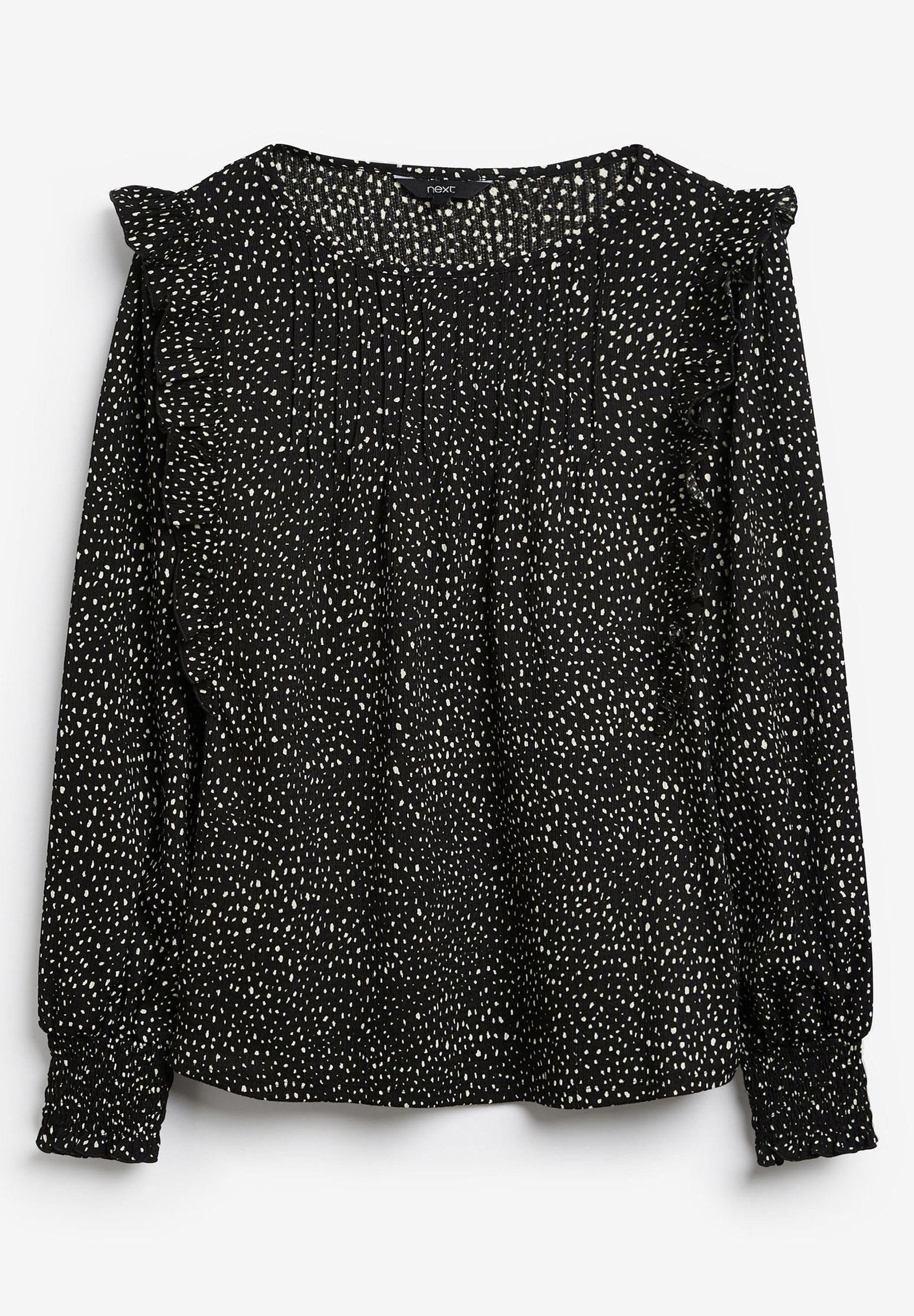 Schwarze Bluse mit einem weiß gesprenkelten Muster, langen Ärmeln, geraffter Textur und Rüschendetails an den Schultern. Gummierte Manschetten.