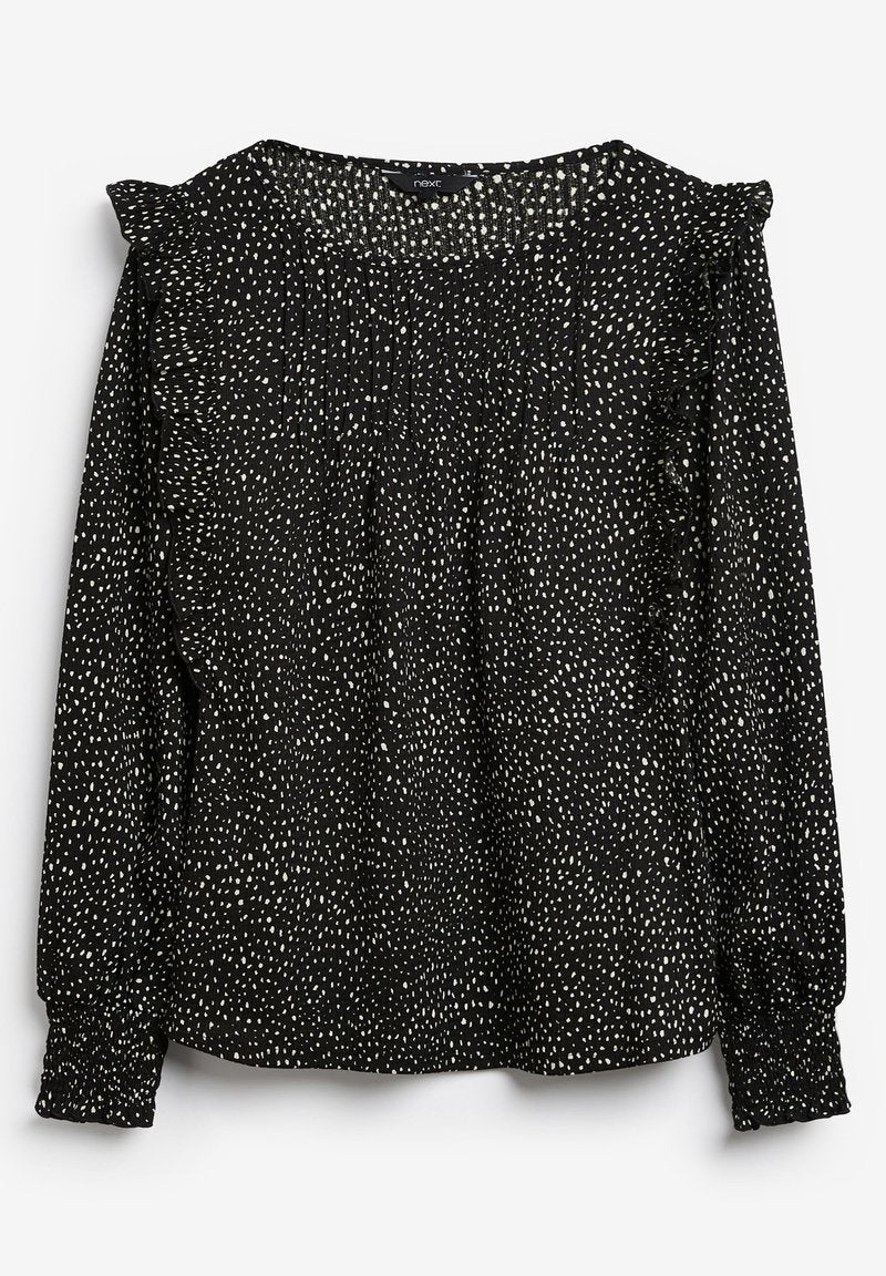 Schwarze Bluse mit einem weiß gesprenkelten Muster, langen Ärmeln, geraffter Textur und Rüschendetails an den Schultern. Gummierte Manschetten.