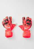 Ein Paar rot-schwarz gemusterte Nike Torwarthandschuhe mit weißen Akzenten und Handgelenkschlaufen, flach auf einer weißen Oberfläche ausgebreitet.