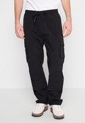 Mann in schwarzen Cargo-Hosen mit Kordelzugbund und weißen Sneakers, der vor einem weißen Hintergrund steht.