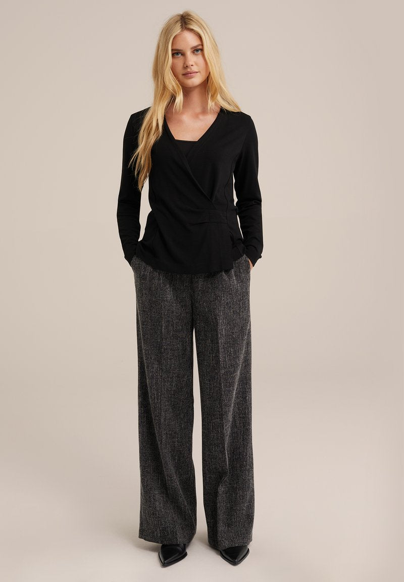 Schwarze Wickelbluse mit langen Ärmeln, kombiniert mit grauen strukturierten weiten Hosen und schwarzen spitzen Pumps. Einfache, klare Linien durchgehend.