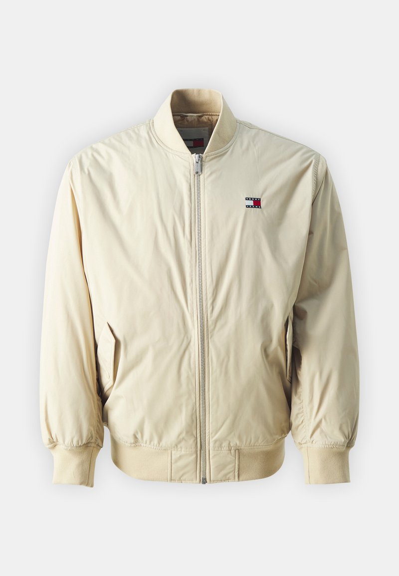 Hellbeige Bomberjacke mit einem Reißverschluss, gerippten Bündchen und Saum. Verfügt über ein kleines Logo-Patch in Rot, Weiß und Blau auf der Brust.
