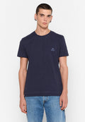 Junger Mann mit kurzen Haaren, der ein navyfarbiges Diesel-T-Shirt und hellblaue Jeans trägt, steht vor einem weißen Hintergrund.