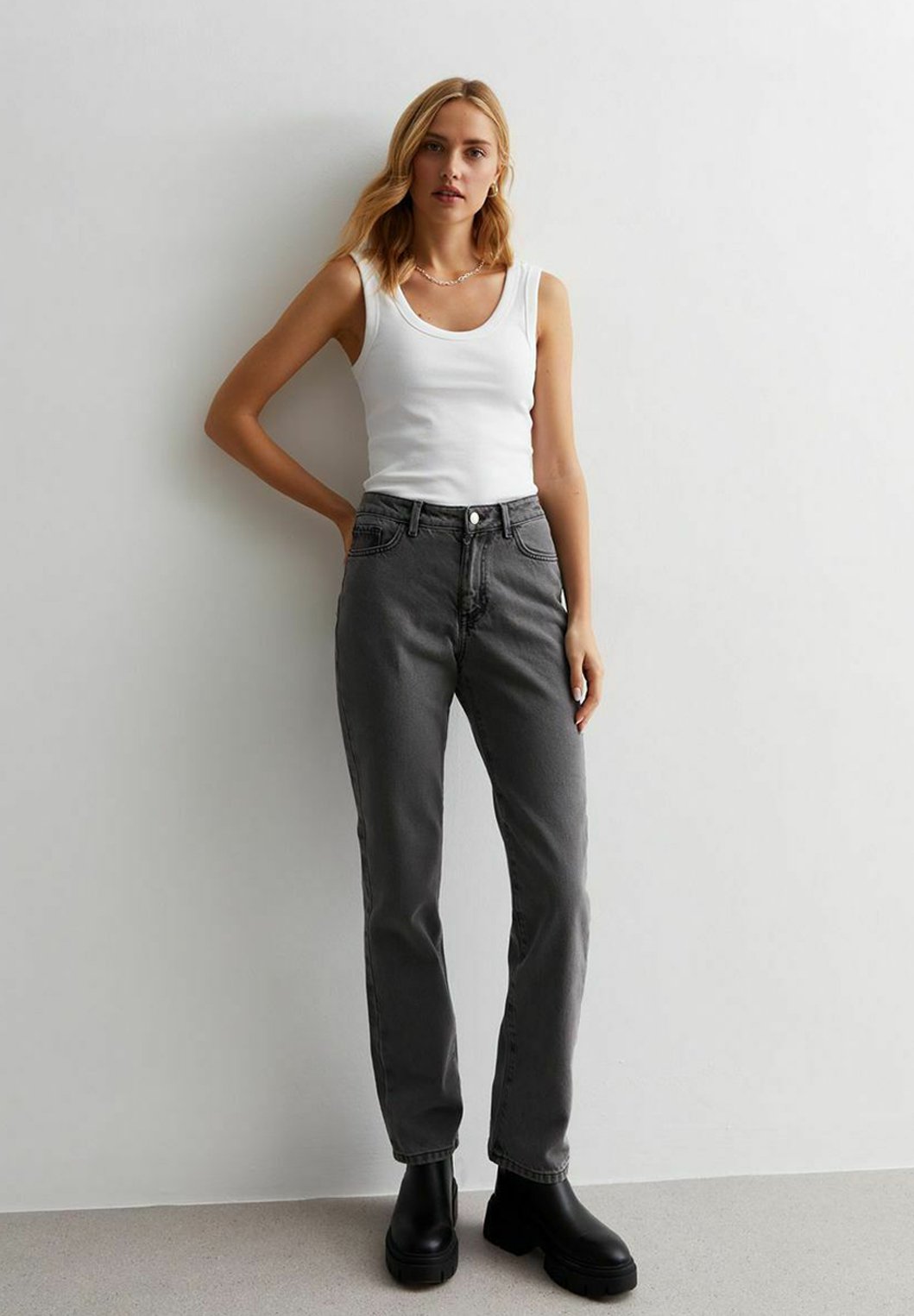 Graue High-Waist-Jeans mit geradem Bein, ausgestattet mit Gürtelschlaufen, vorderen Taschen und einem Knopfverschluss, kombiniert mit einem enganliegenden weißen Tanktop.