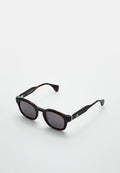 Schildpatt-Sonnenbrille mit dunklen Gläsern, rechteckiger Form, dicken Rahmen und metallischen Akzenten an den Bügeln.